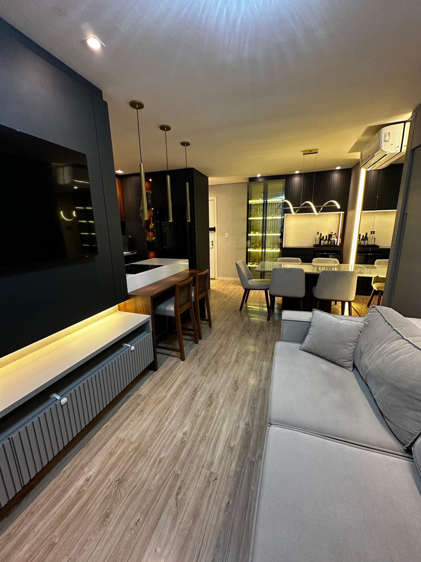 Sala de estar integrada à cozinha e sala de jantar, com painel de TV e bancada de refeições