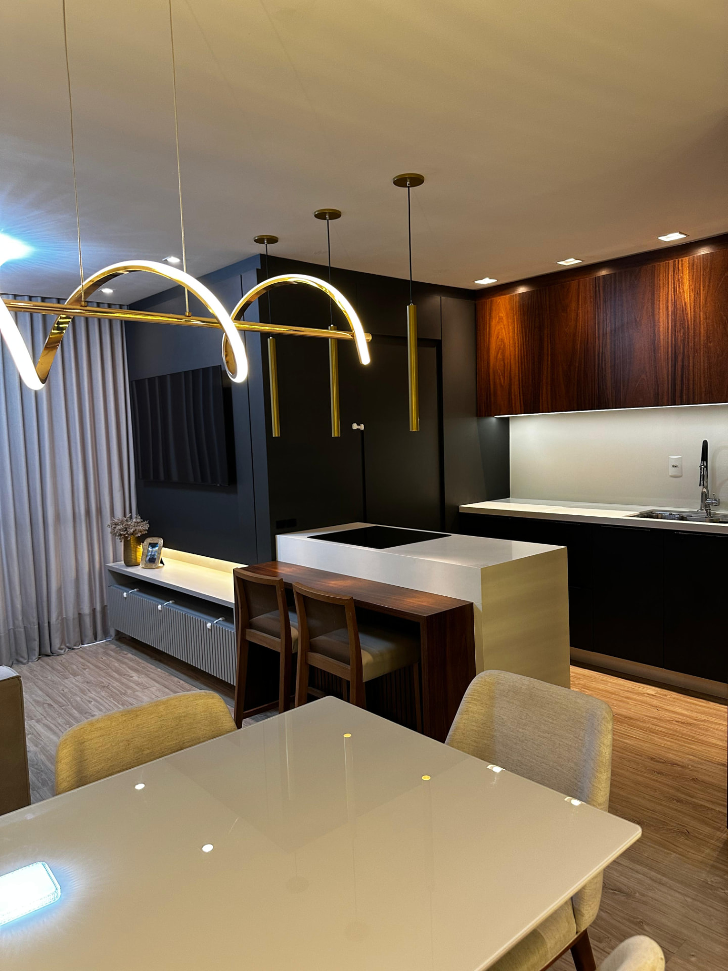 Cozinha com ilha, cooktop, armários em madeira nobre e projeto luminotécnico em dourado