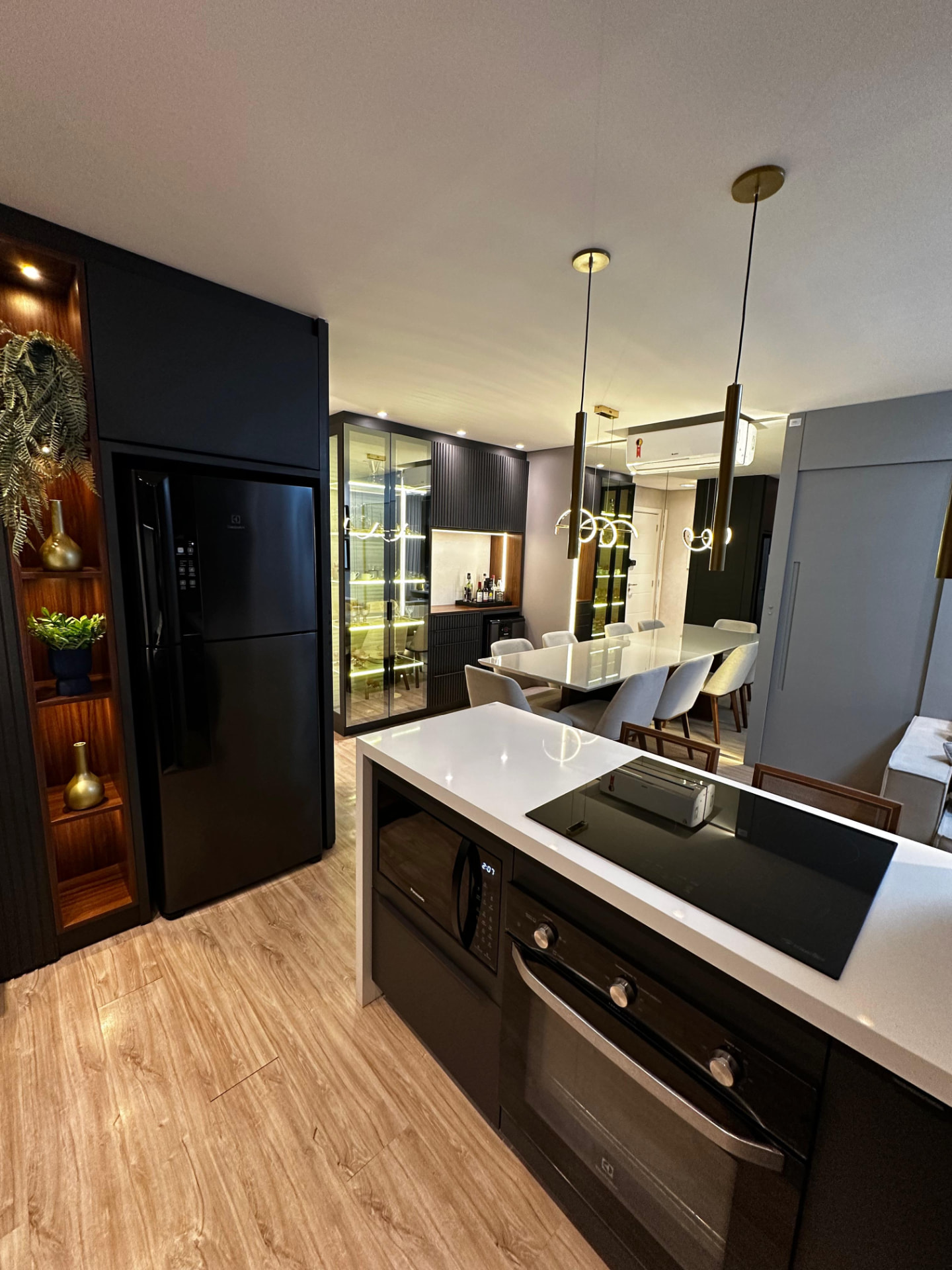 Cozinha planejada em tom escuro com cristaleira iluminada e mesa de jantar ao fundo