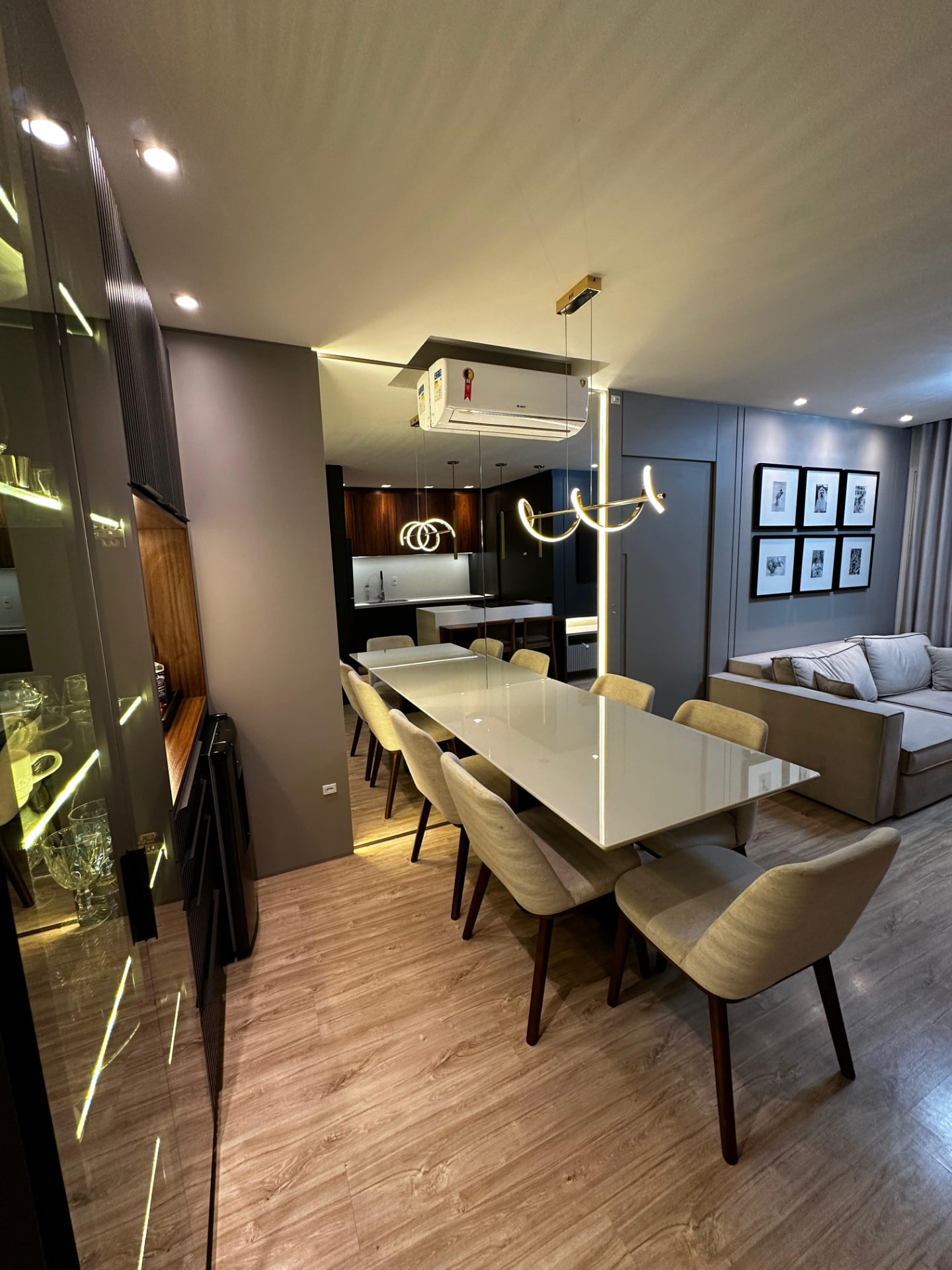 Sala de jantar com mesa para oito lugares, pendente de design e cristaleira iluminada