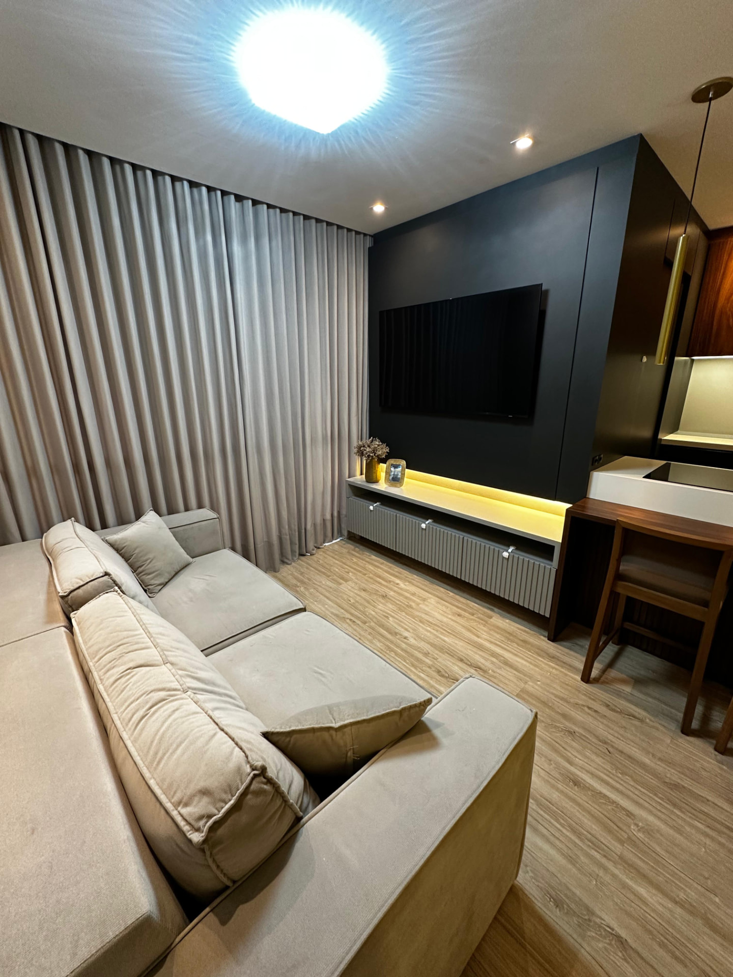 Sala de estar com sofá retrátil, cortina em todo o vão e painel de TV com iluminação embutida